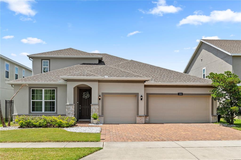 A two-story suburban house features a three-car garage, stone accents, and a brick paver driveway — 3385 WAUSEON DRIVE, ST CLOUD, FL