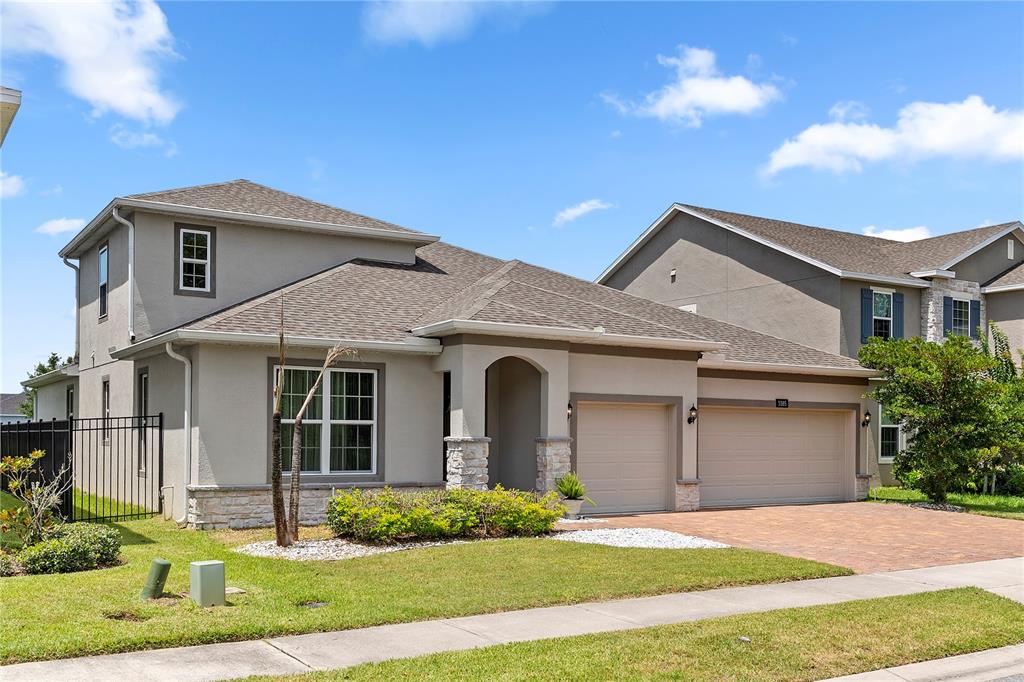A two-story suburban house with a beige stucco exterior, stone accents, and a two-car garage — 3385 WAUSEON DRIVE, ST CLOUD, FL