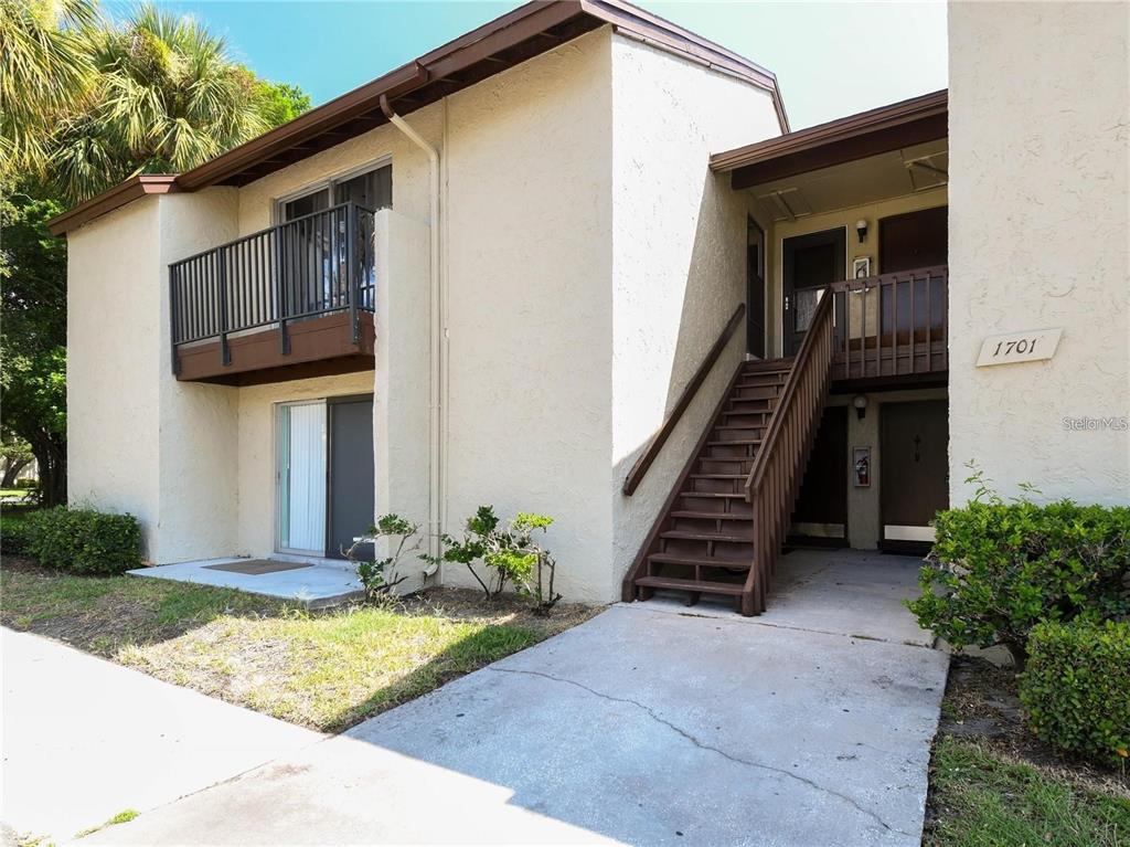 A two-story stucco apartment building features an exterior wooden staircase and a second-floor balcony — 4215 E BAY DRIVE UNIT 1701B, CLEARWATER, FL