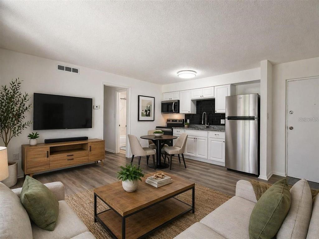 A living room and kitchen area with white cabinets, stainless steel appliances, and wood flooring — 4215 E BAY DRIVE UNIT 1701B, CLEARWATER, FL