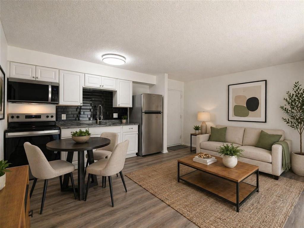 An open-concept living room and kitchen featuring white cabinets, stainless appliances, and wood-look flooring — 4215 E BAY DRIVE UNIT 1701B, CLEARWATER, FL