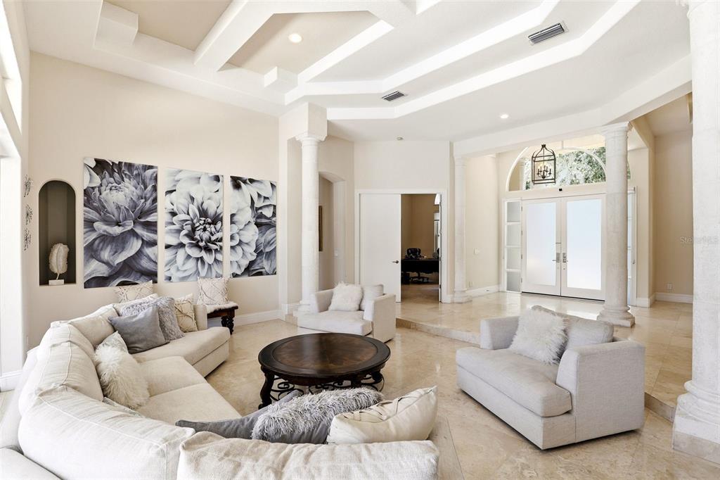 A spacious living room features a coffered ceiling, stone columns, and large black-and-white floral art — 9151 POINT CYPRESS DRIVE, ORLANDO, FL