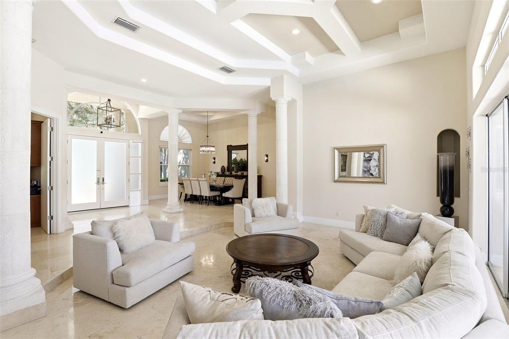 A spacious living room with high coffered ceilings, stone floors, and an adjacent dining area — 9151 POINT CYPRESS DRIVE, ORLANDO, FL