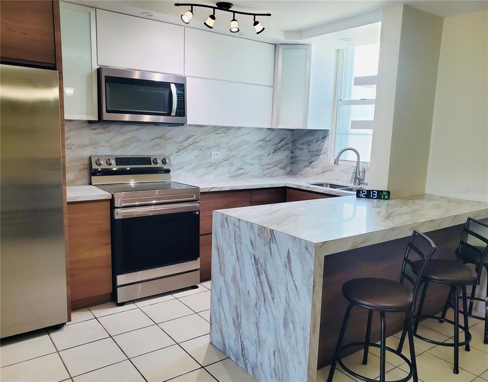 A modern kitchen features white upper cabinets, wood lower cabinets, and marble-patterned countertops and backsplash — La Loma 104, FAJARDO, PR