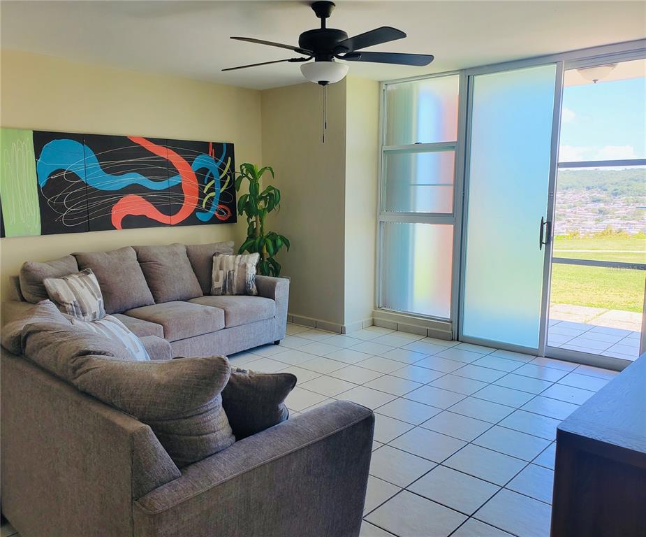 A living room with a gray sectional sofa, abstract wall art, and sliding glass balcony doors — La Loma 104, FAJARDO, PR