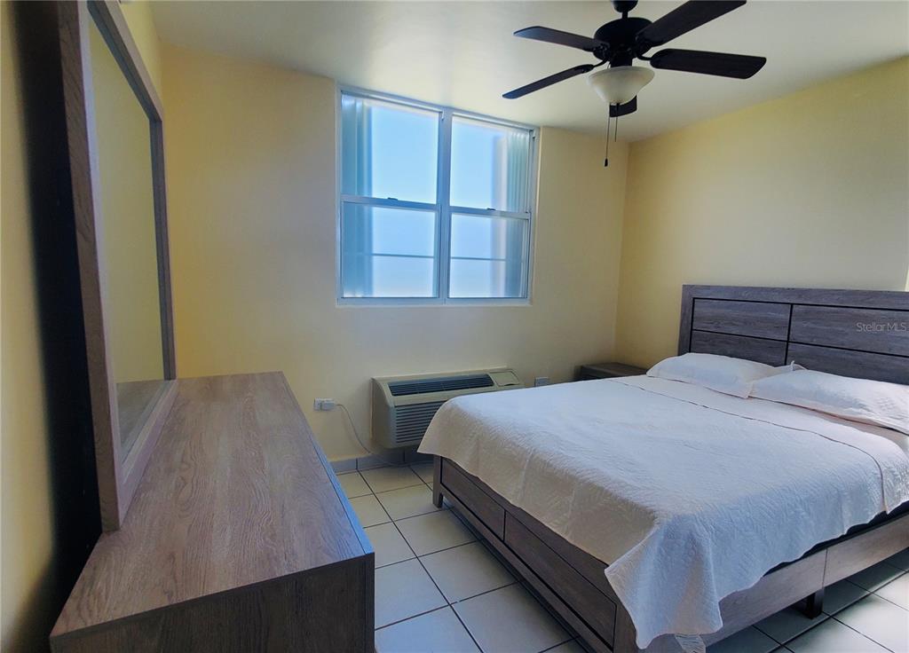 A bedroom features a bed, a dresser with a mirror, tile floors, and a window — La Loma 104, FAJARDO, PR