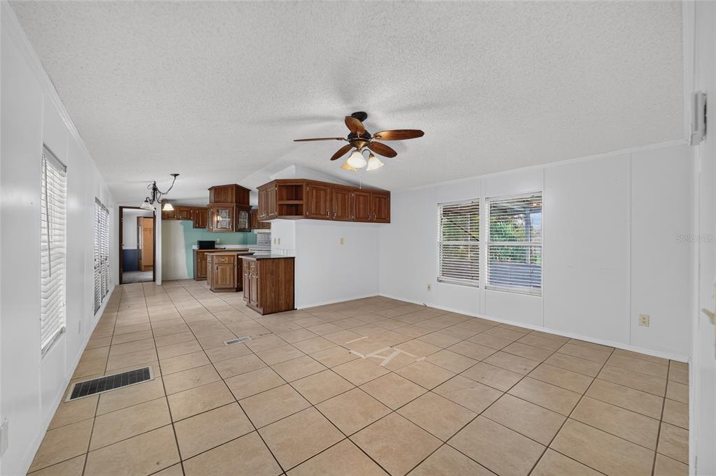 An open-concept room features light-colored tile flooring, white walls, and a wooden kitchen area — 14085 SE 59TH COURT, SUMMERFIELD, FL