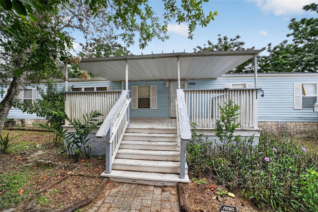 A light blue mobile home features a wooden front deck with stairs and a metal awning — 14085 SE 59TH COURT, SUMMERFIELD, FL