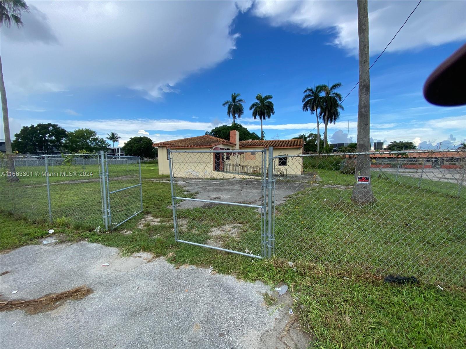 A single-story house with a tile roof sits behind a chain-link fence and gate — 13400 Alexandria Dr, Opa-Locka FL 33054, OPA-LOCKA, FL
