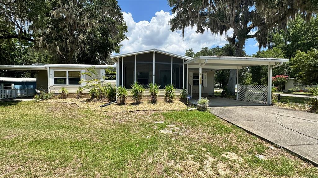 A single-story mobile home features a screened front porch, a carport, and mature oak trees — 1913 NW 47TH TERRACE, OCALA, FL