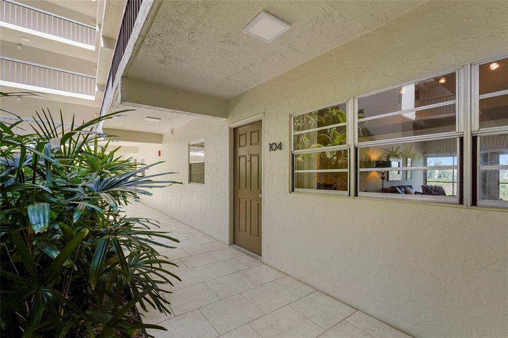An exterior view of a ground-level apartment entrance with a brown door numbered 104 — 3240 GULF OF MEXICO DRIVE UNIT B104, LONGBOAT KEY, FL