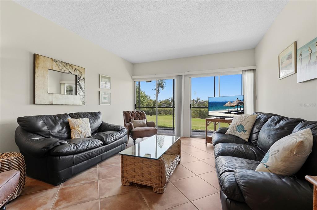 A living room features two black leather sofas, a glass-topped wicker coffee table, and sliding doors — 3240 GULF OF MEXICO DRIVE UNIT B104, LONGBOAT KEY, FL