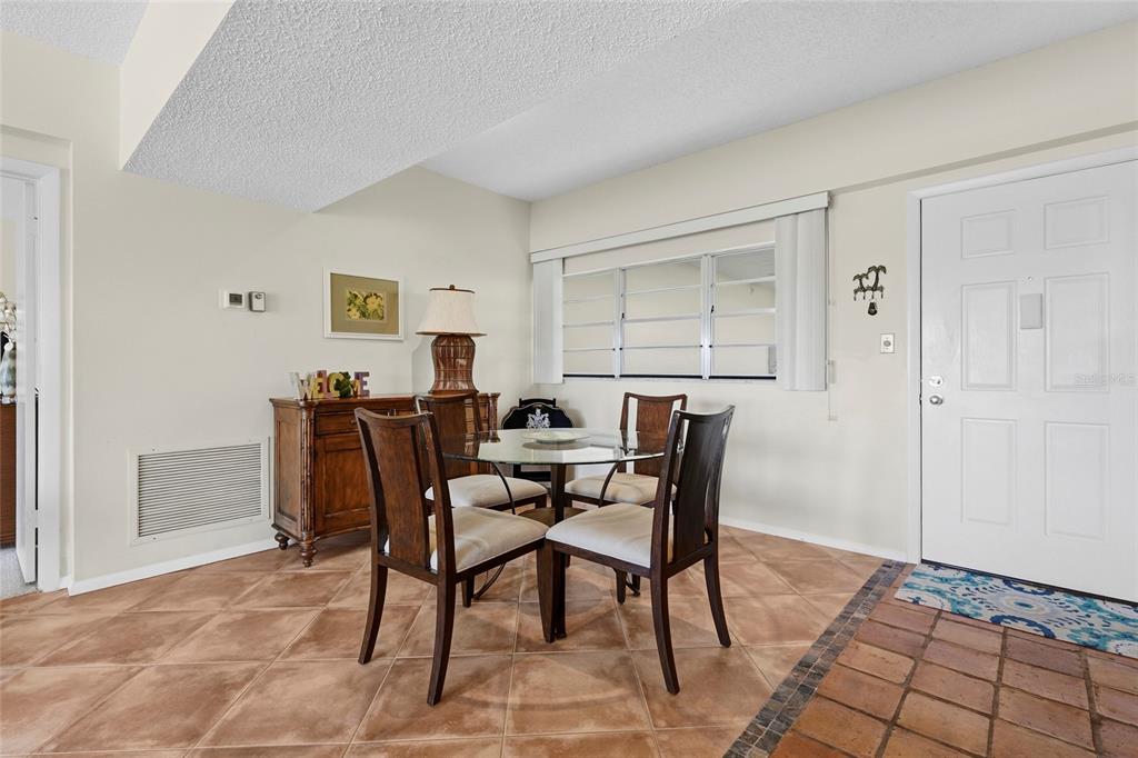 A dining area features a glass table, four wooden chairs, tile flooring, and a white door — 3240 GULF OF MEXICO DRIVE UNIT B104, LONGBOAT KEY, FL