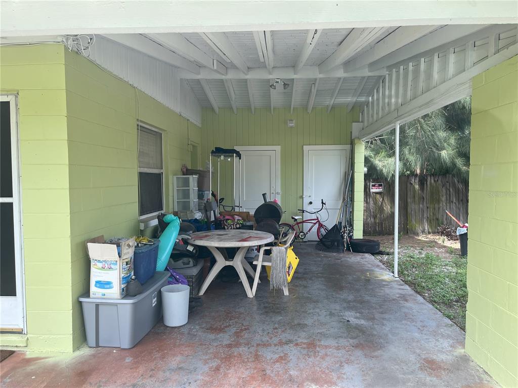 A covered concrete patio features light green block walls, a white ceiling, and various stored items — 1528 STEVENSONS DRIVE, CLEARWATER, FL