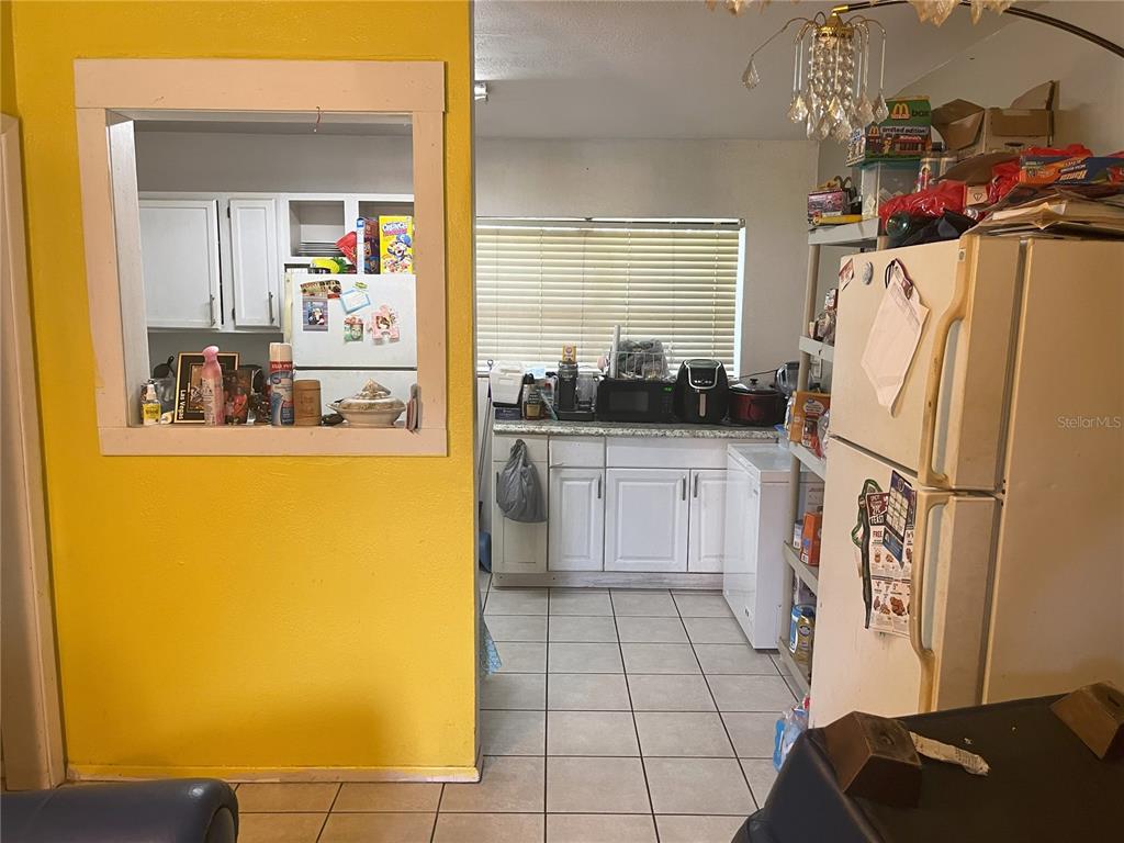 A kitchen with white cabinets, tile flooring, and a pass-through window to an adjacent room — 1528 STEVENSONS DRIVE, CLEARWATER, FL