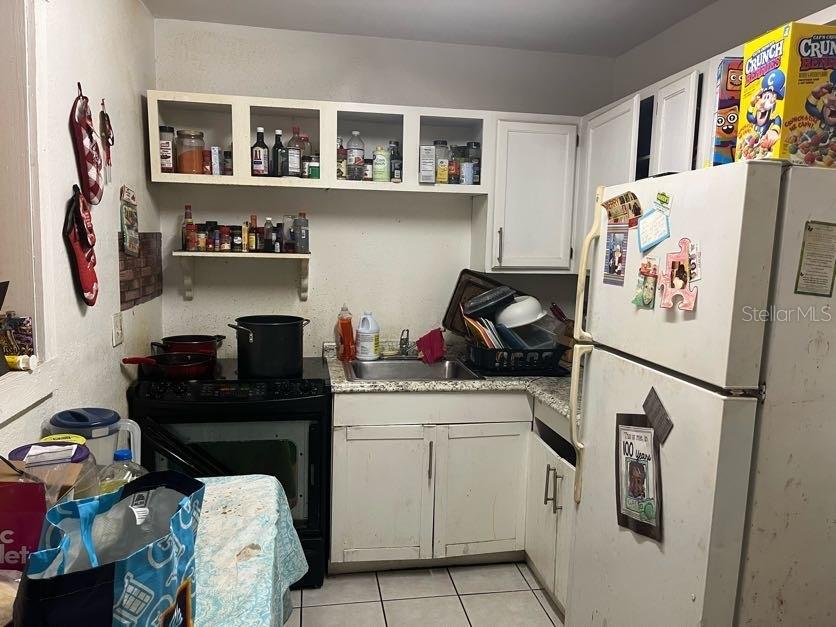 A small kitchen features white cabinets, a black stove, a stainless steel sink, and appliances — 1528 STEVENSONS DRIVE, CLEARWATER, FL