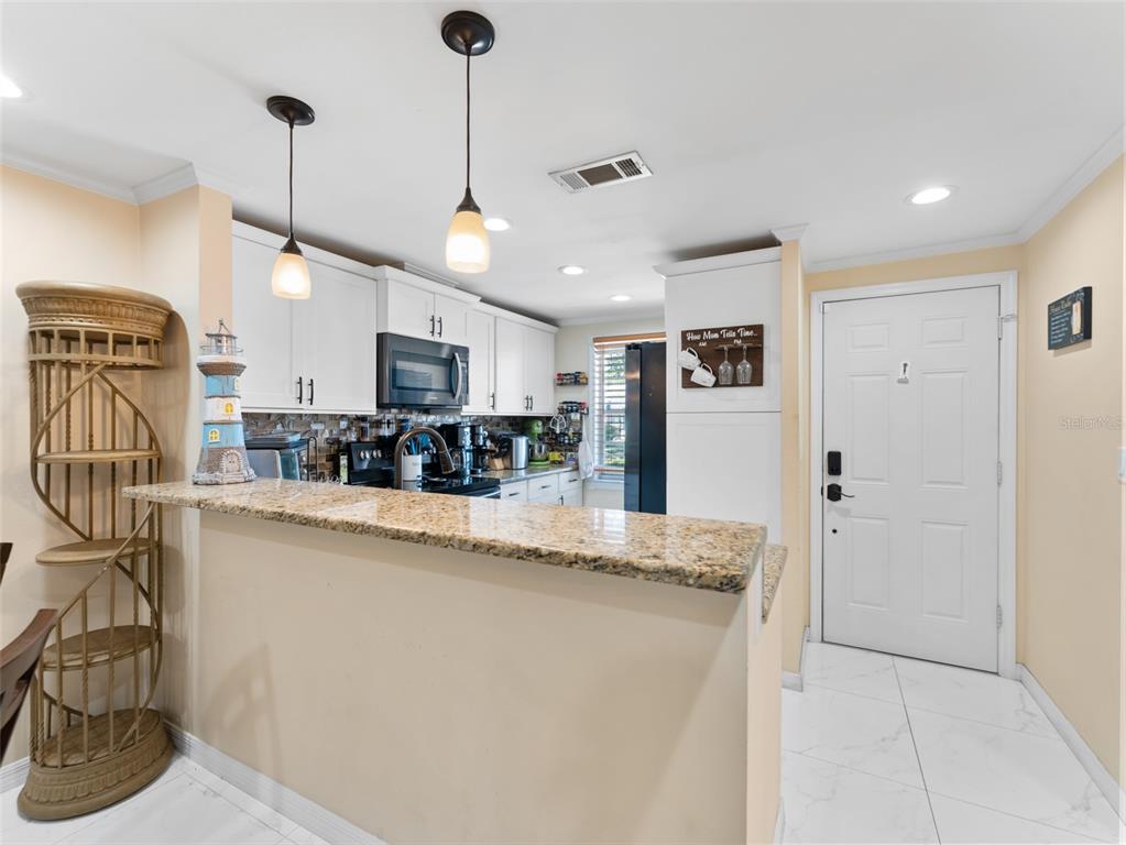 A kitchen features white cabinets, granite countertops, a breakfast bar, and a white entry door — 4237 REDCLIFF PLACE UNIT -, NEW PORT RICHEY, FL