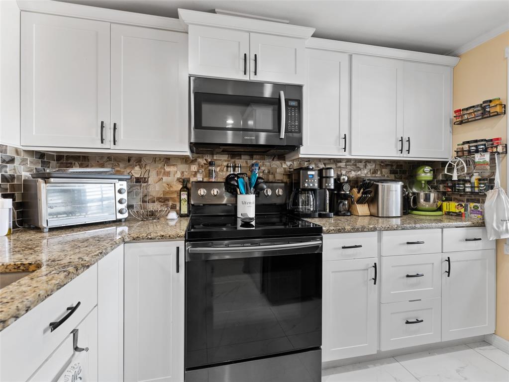 A kitchen features white cabinets, granite countertops, a tiled backsplash, and stainless steel appliances — 4237 REDCLIFF PLACE UNIT -, NEW PORT RICHEY, FL