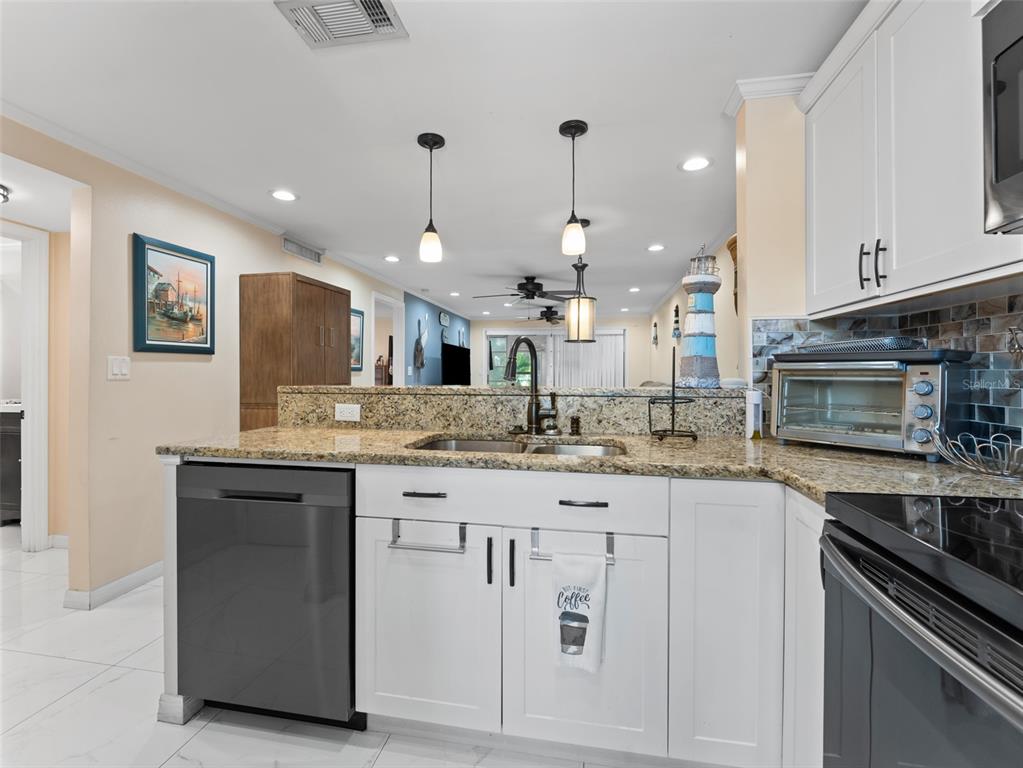 A kitchen features white cabinets, granite countertops, a stainless steel dishwasher, and pendant lighting — 4237 REDCLIFF PLACE UNIT -, NEW PORT RICHEY, FL