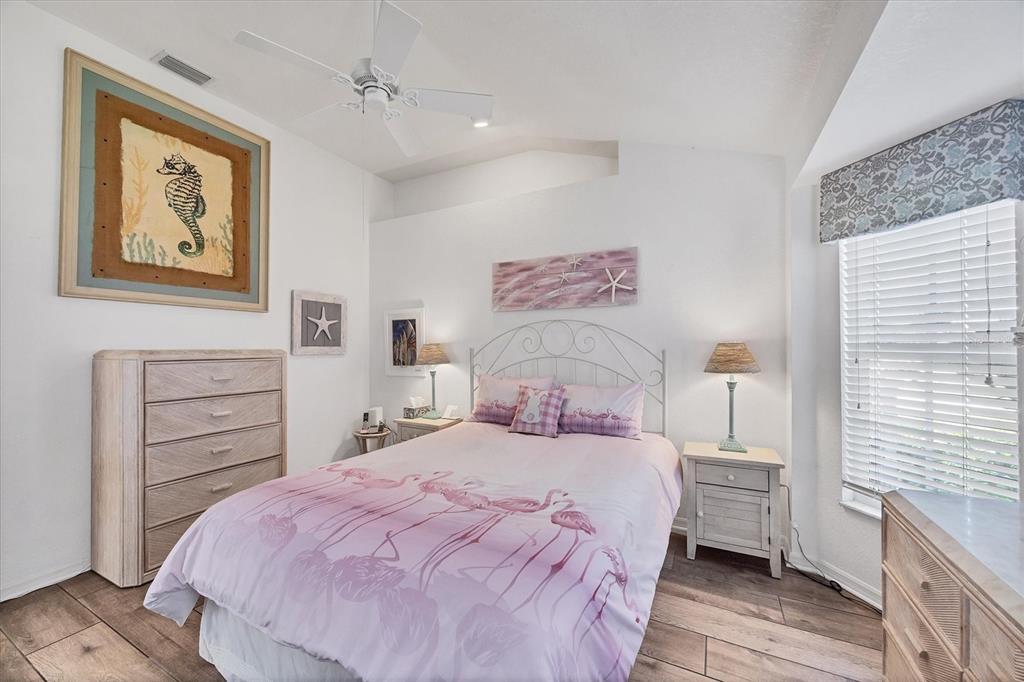 A bedroom features a flamingo-patterned bed, white furniture, a ceiling fan, and coastal-themed wall art — 11 AMBERJACK LANE, PLACIDA, FL