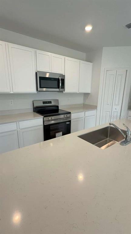 A kitchen features white cabinetry, stainless steel appliances, and a light-colored quartz island countertop — 3619 HARDMAN DRIVE, LAKE WALES, FL