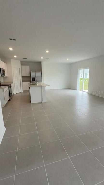 A bright, open-concept kitchen and living area features white cabinetry, an island, and tile flooring — 3619 HARDMAN DRIVE, LAKE WALES, FL