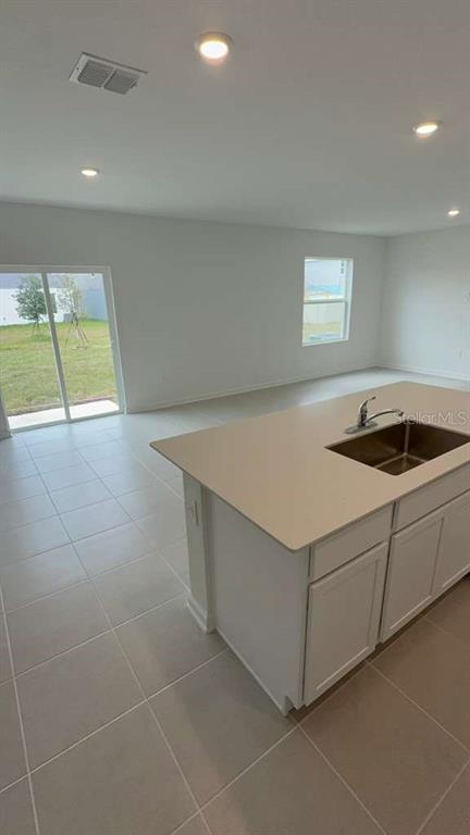 A kitchen island with a sink sits in a room with white cabinets and tile floors — 3619 HARDMAN DRIVE, LAKE WALES, FL