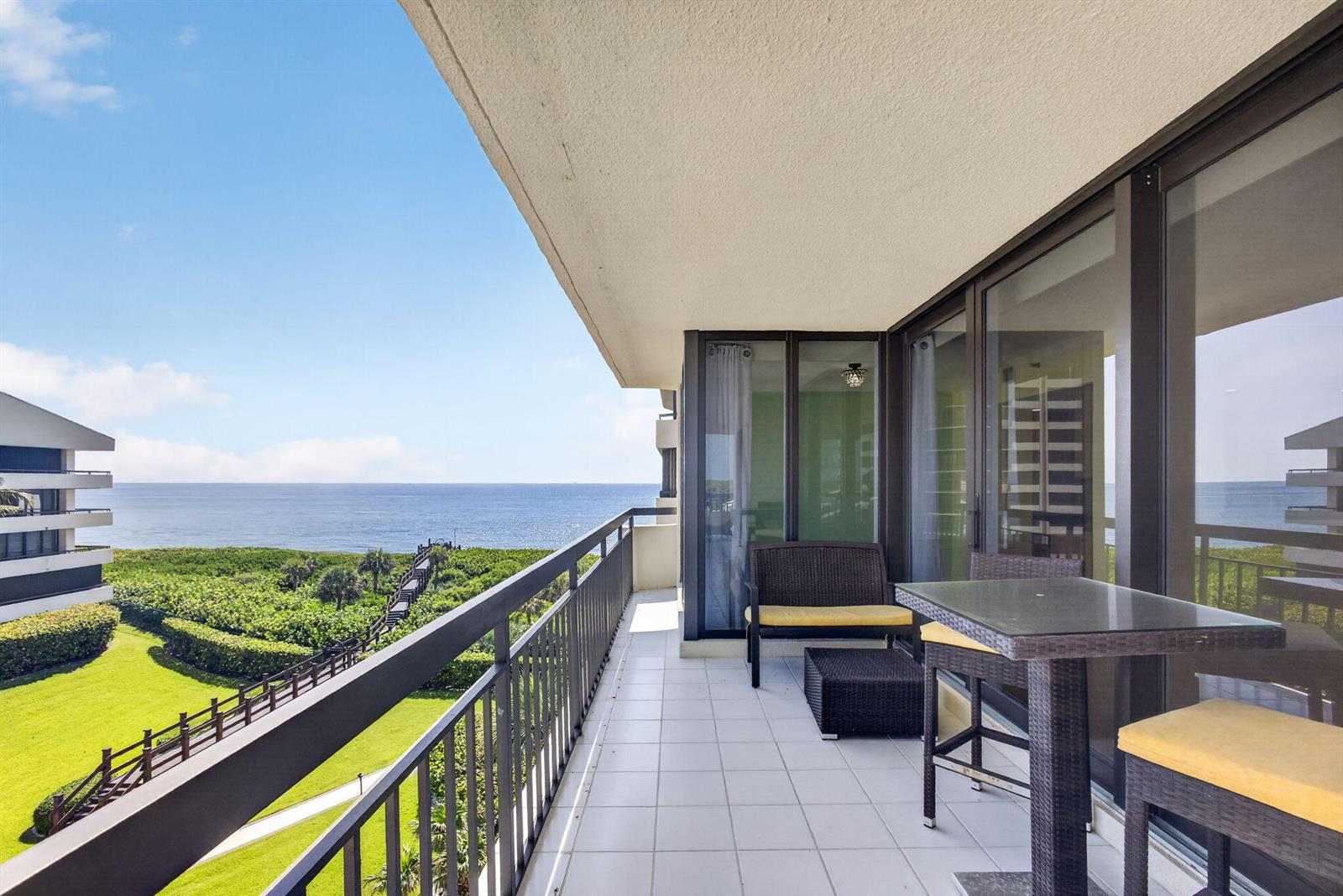 A balcony with outdoor furniture overlooks a grassy lawn, a wooden walkway, and the ocean — 4000 N Ocean Drive # 403, Singer Island FL 33404, SINGER ISLAND, FL