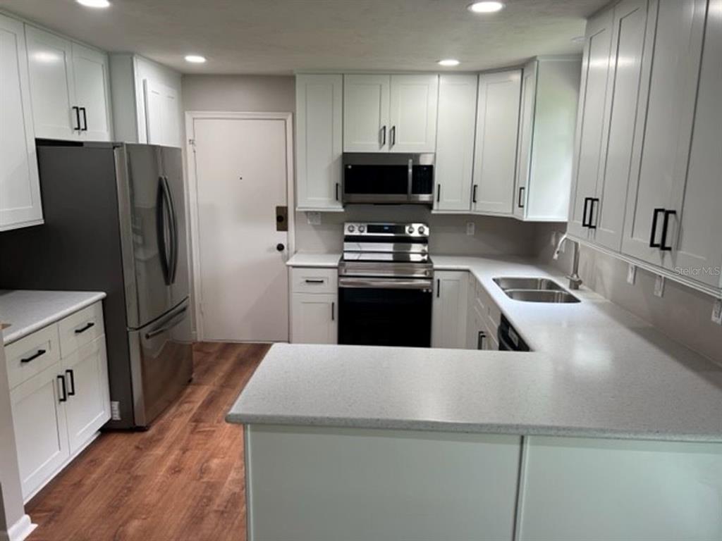 A kitchen features white cabinetry, stainless steel appliances, light countertops, and wood-look flooring — 6613 NW 30TH TERRACE, GAINESVILLE, FL