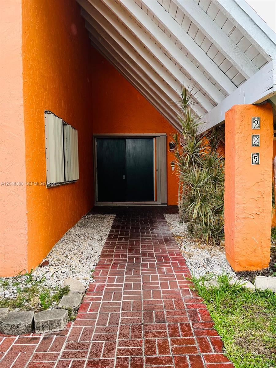 A brick walkway leads to a dark double-door entrance under a bright orange exterior — 925 NE 207th Ter # 0, Miami FL 33179, MIAMI, FL