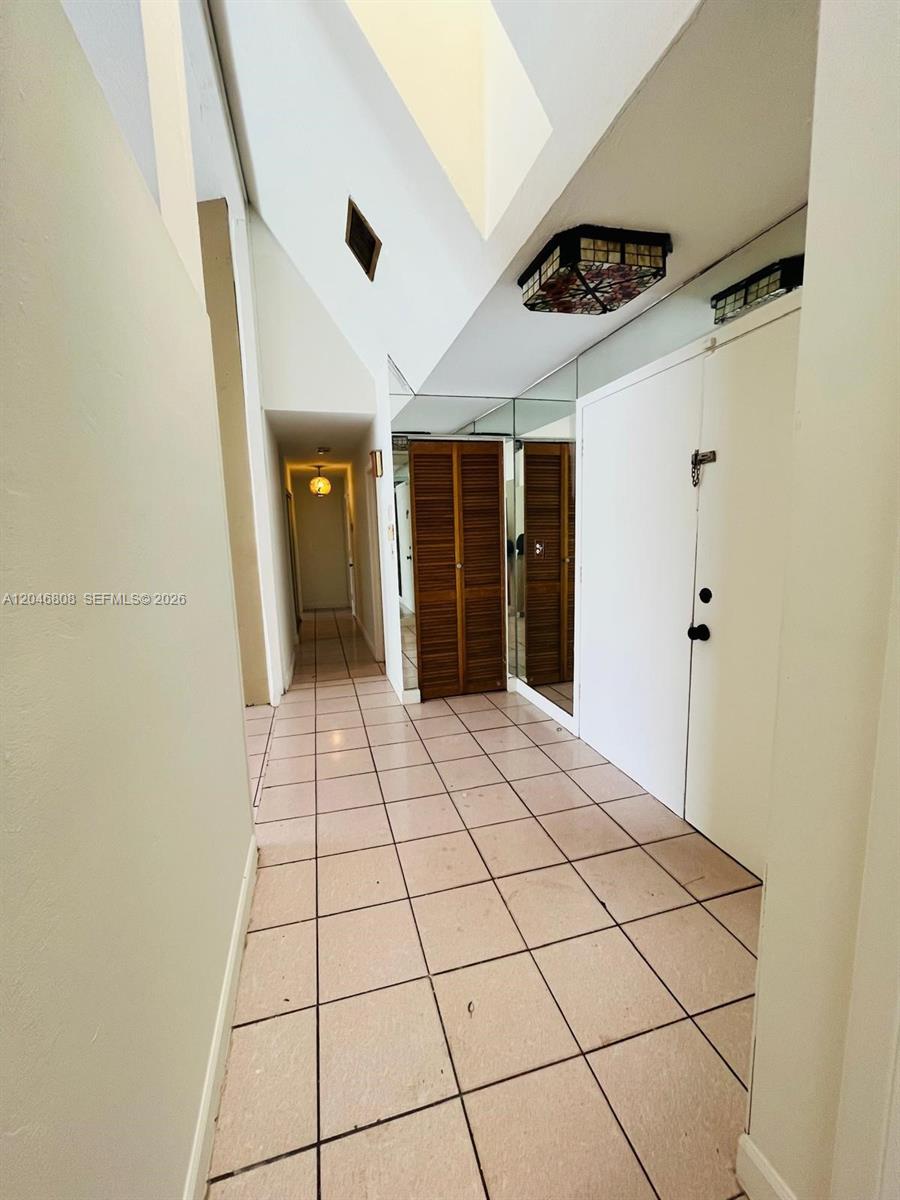 A tiled hallway features a vaulted ceiling, mirrored closet doors, and a decorative light fixture — 925 NE 207th Ter # 0, Miami FL 33179, MIAMI, FL