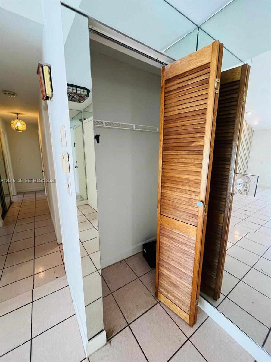 A hallway with tiled floors features a closet with wooden louvered doors and mirrored walls — 925 NE 207th Ter # 0, Miami FL 33179, MIAMI, FL