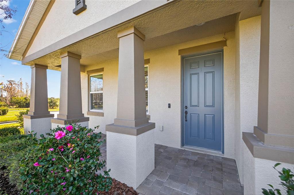 A covered front porch with stone pavers, square columns, and a blue front door — 17268 BRIGHTON LAKE ROAD, LAND O LAKES, FL