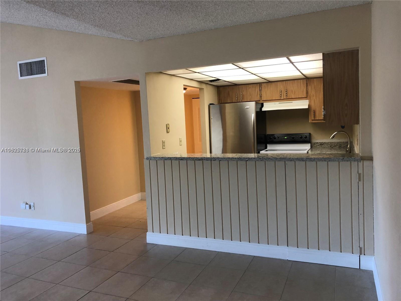A kitchen with stainless steel appliances and a breakfast bar overlooks a tiled living area — 5995 Washington St # 233, Hollywood FL 33023, HOLLYWOOD, FL