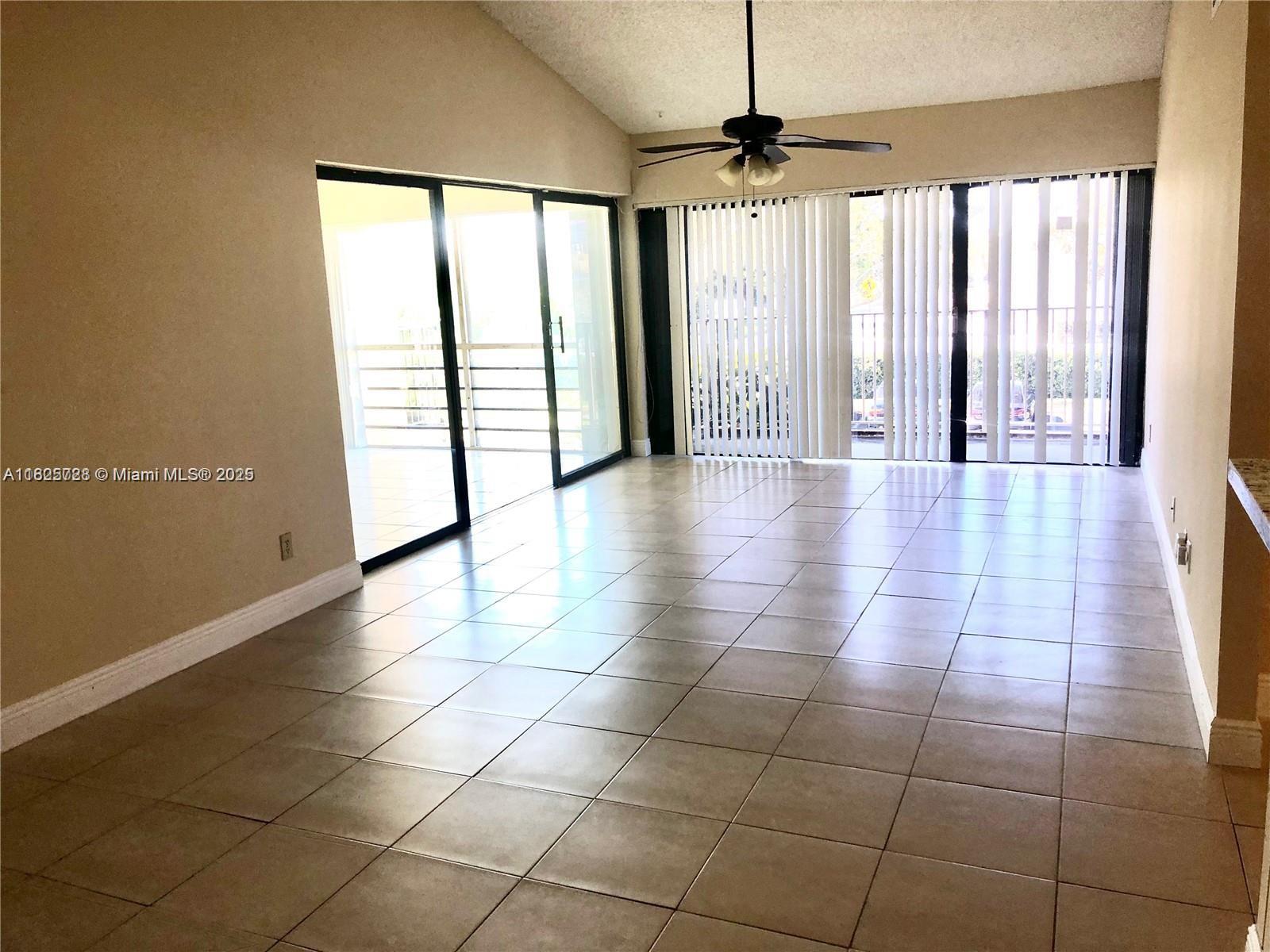 A living room with beige tile flooring, a vaulted ceiling, and sliding glass balcony doors — 5995 Washington St # 233, Hollywood FL 33023, HOLLYWOOD, FL
