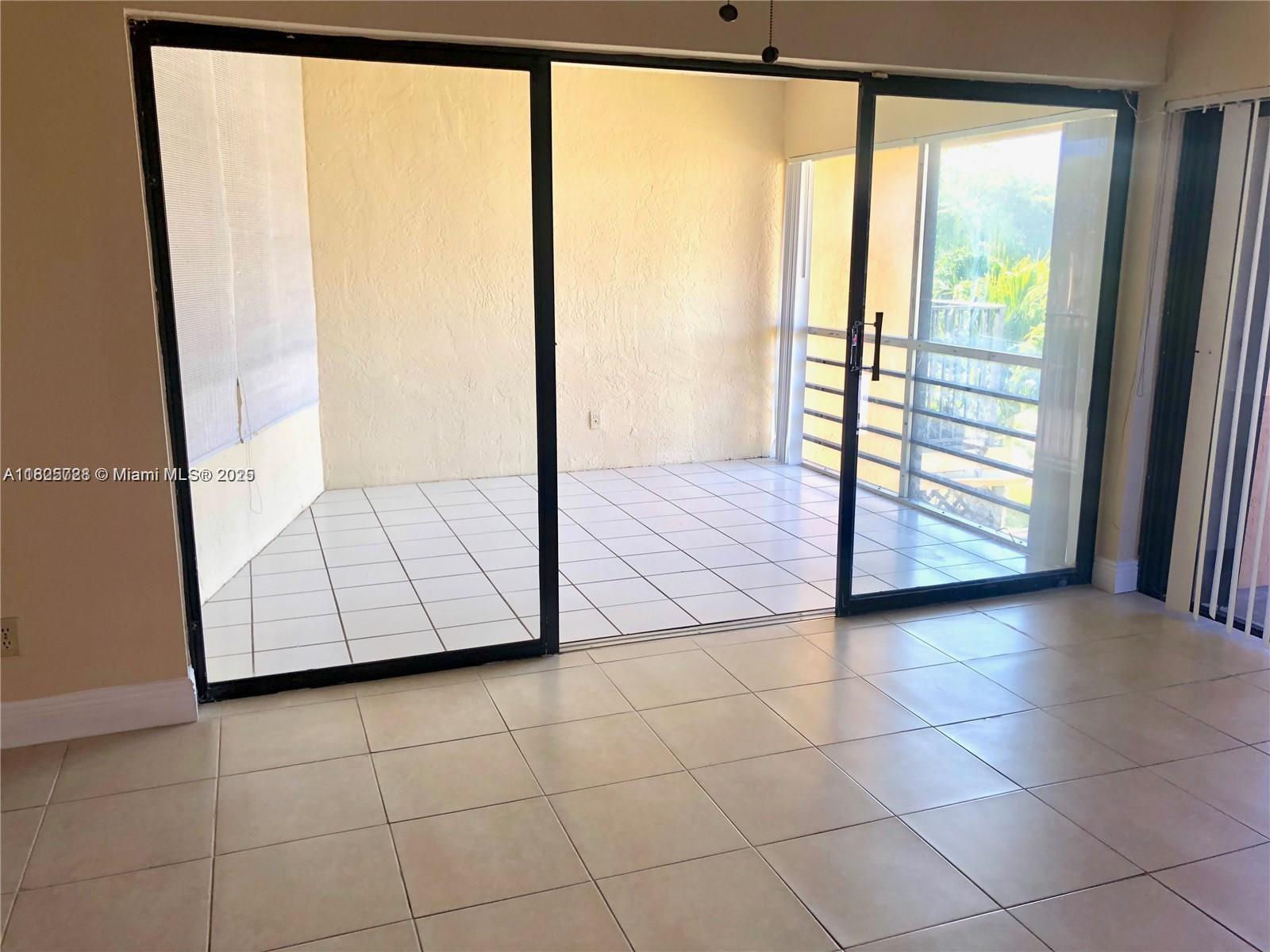 A tiled room features a large sliding glass door opening onto a screened-in balcony — 5995 Washington St # 233, Hollywood FL 33023, HOLLYWOOD, FL