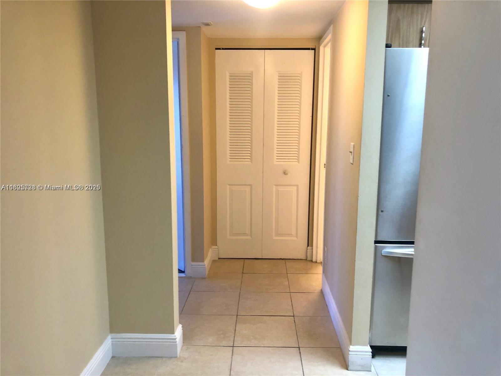 A hallway with beige tile flooring leads to a white louvered closet door — 5995 Washington St # 233, Hollywood FL 33023, HOLLYWOOD, FL