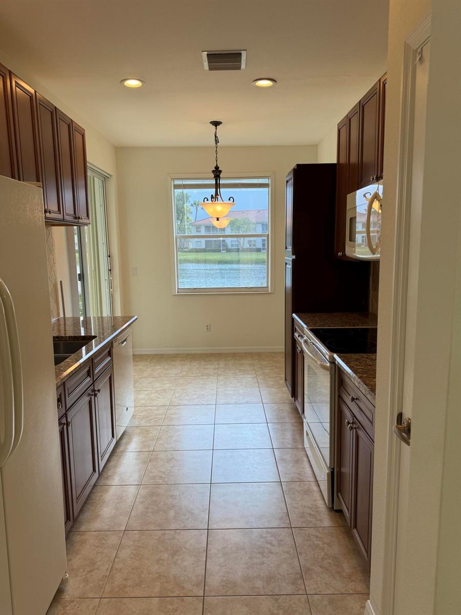 A galley kitchen features dark wood cabinets, granite countertops, and a window overlooking a lake — 2140 Wingate Bend, Wellington FL 33414, WELLINGTON, FL
