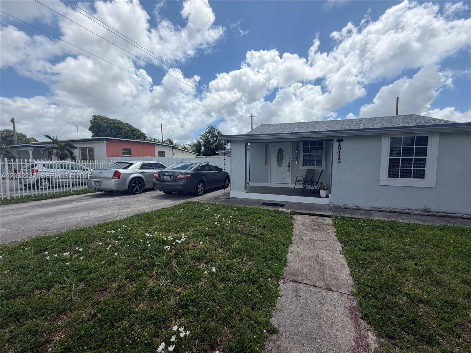 A single-story house with a gray exterior, a front porch, and two cars parked in the driveway — 10415 NW 30th Ct, Miami FL 33147, MIAMI, FL