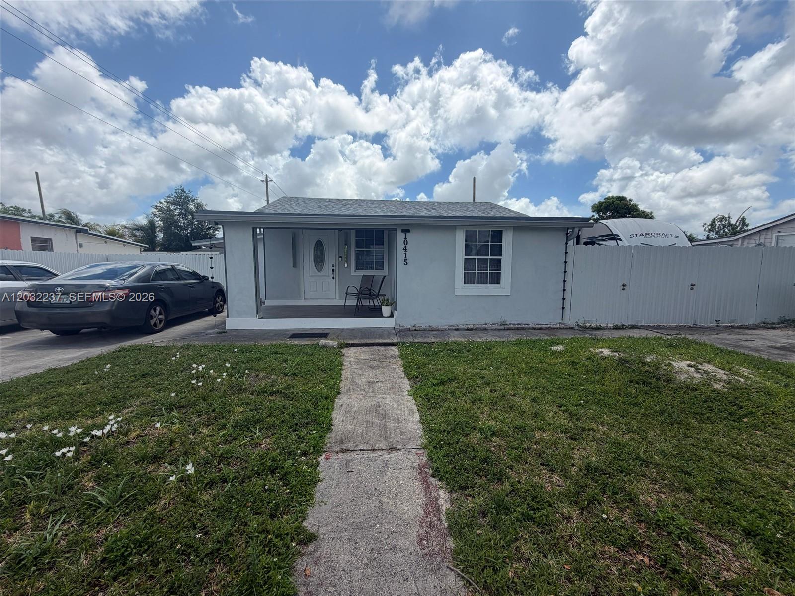 A single-story house with a front porch, white fence, and a car parked in the driveway — 10415 NW 30th Ct, Miami FL 33147, MIAMI, FL