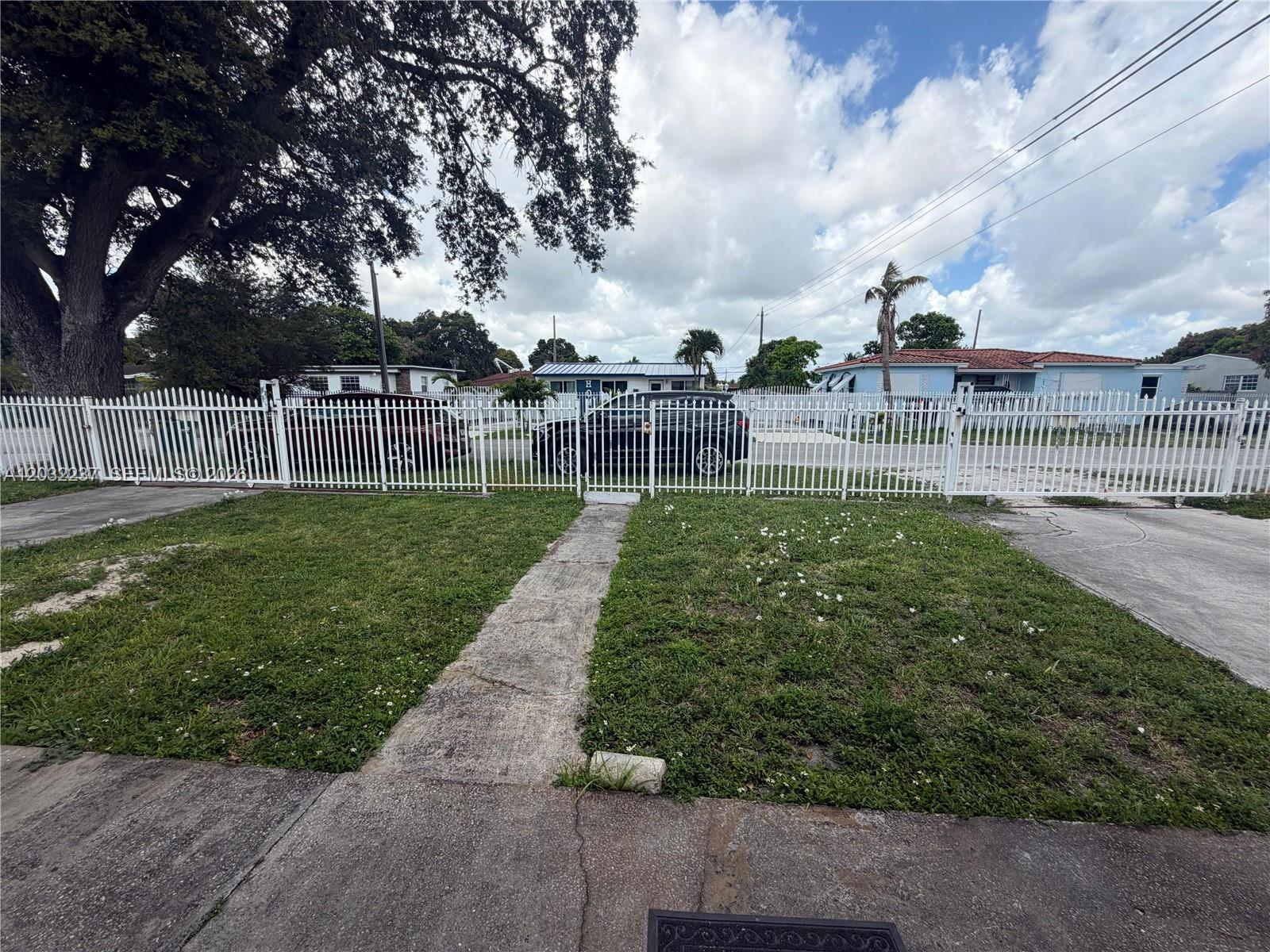 A white metal fence encloses a front yard with a concrete walkway and grass — 10415 NW 30th Ct, Miami FL 33147, MIAMI, FL
