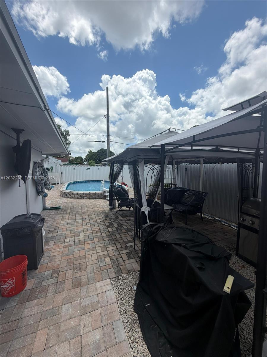 A paved backyard patio features a gazebo, outdoor seating, a grill, and an above-ground pool — 10415 NW 30th Ct, Miami FL 33147, MIAMI, FL