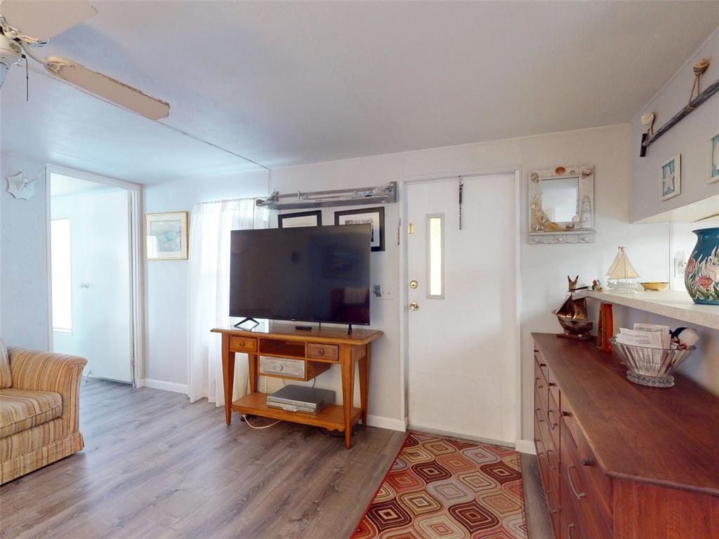 A living room with wood-look flooring, a television on a wooden stand, and an entryway door — 2201 S RIDGEWOOD AVENUE UNIT 8, EDGEWATER, FL
