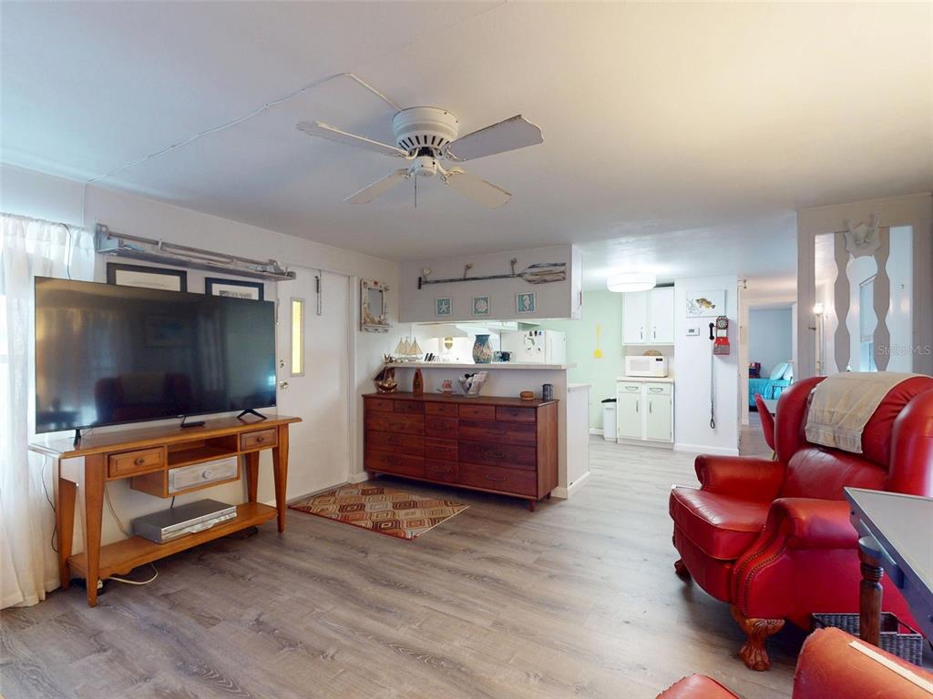 A living room features wood-look flooring, a ceiling fan, a television console, and a red chair — 2201 S RIDGEWOOD AVENUE UNIT 8, EDGEWATER, FL