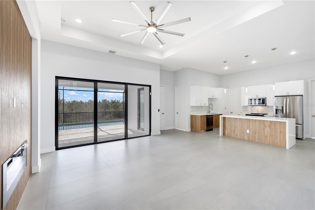 A modern open-concept living area features a kitchen with wood-tone cabinetry and sliding glass doors — 14431 ARTESIA AVENUE, PORT CHARLOTTE, FL