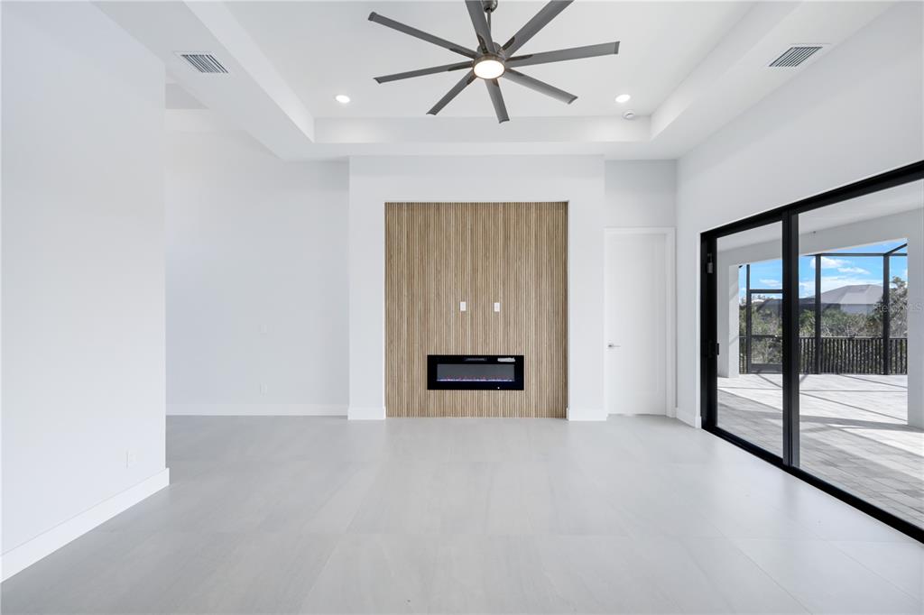A modern living room features a wood-slat accent wall with an electric fireplace and sliding doors — 14431 ARTESIA AVENUE, PORT CHARLOTTE, FL