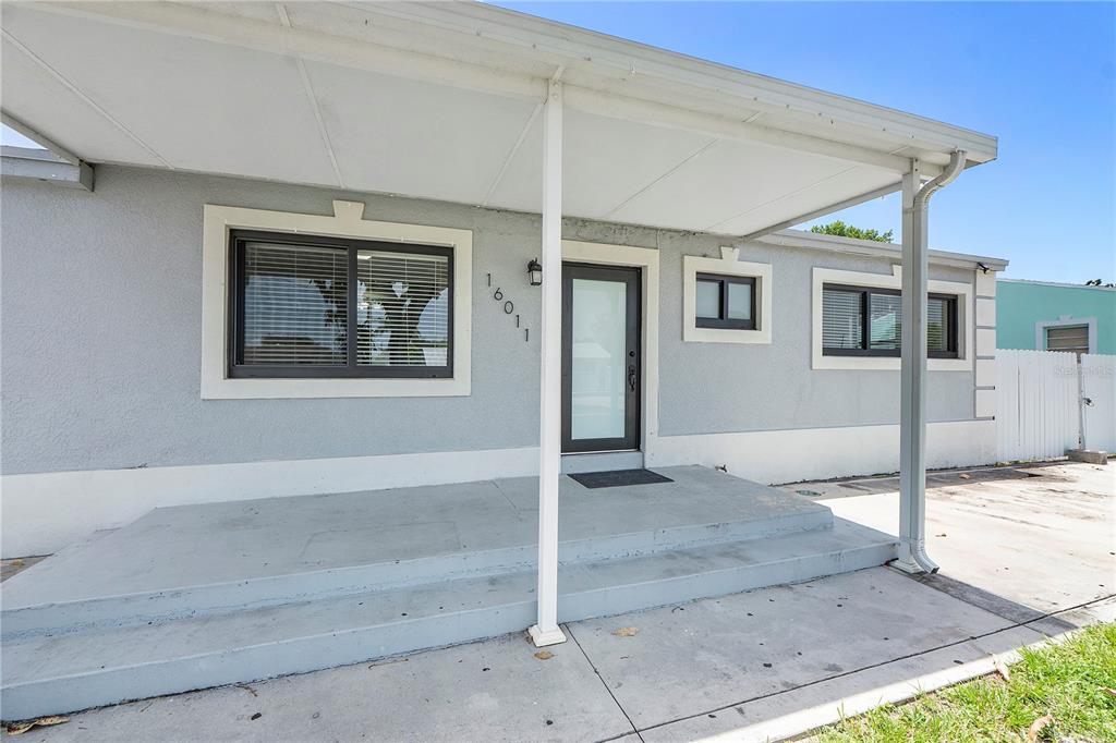A gray house exterior features a covered concrete porch, a front door, and several windows — 16011 NW 40TH COURT, MIAMI GARDENS, FL