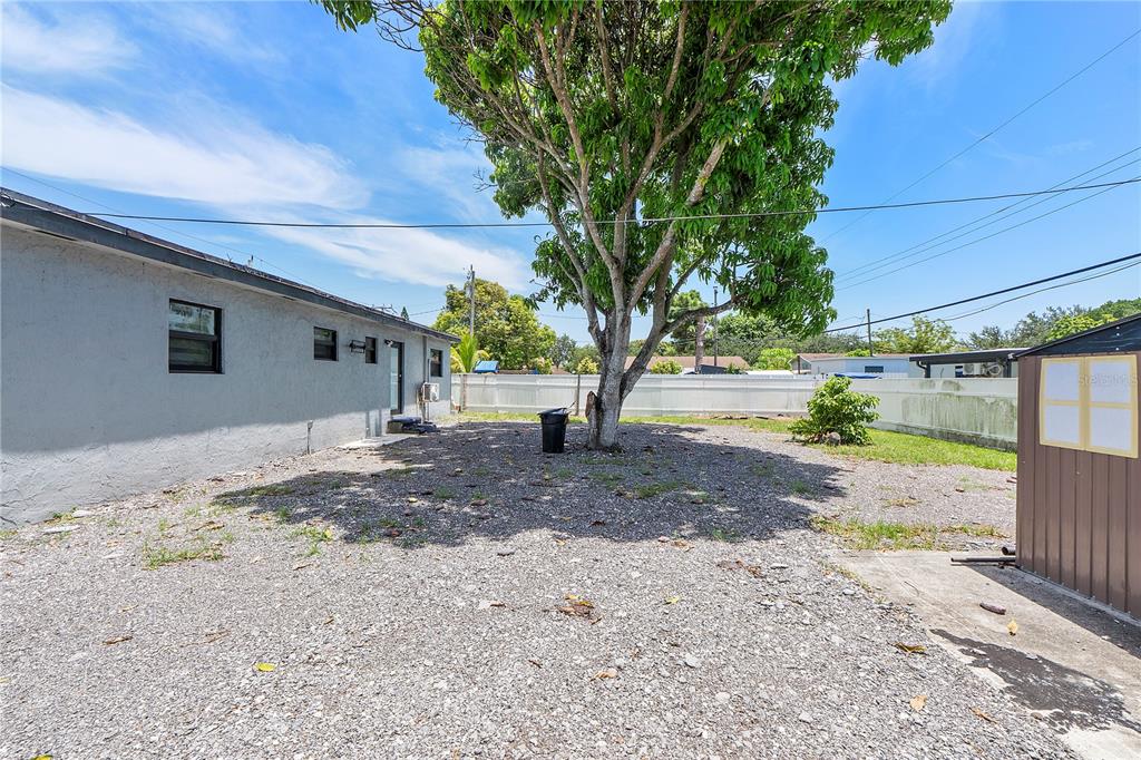 A gravel backyard features a large tree, a gray house exterior, and a storage shed — 16011 NW 40TH COURT, MIAMI GARDENS, FL