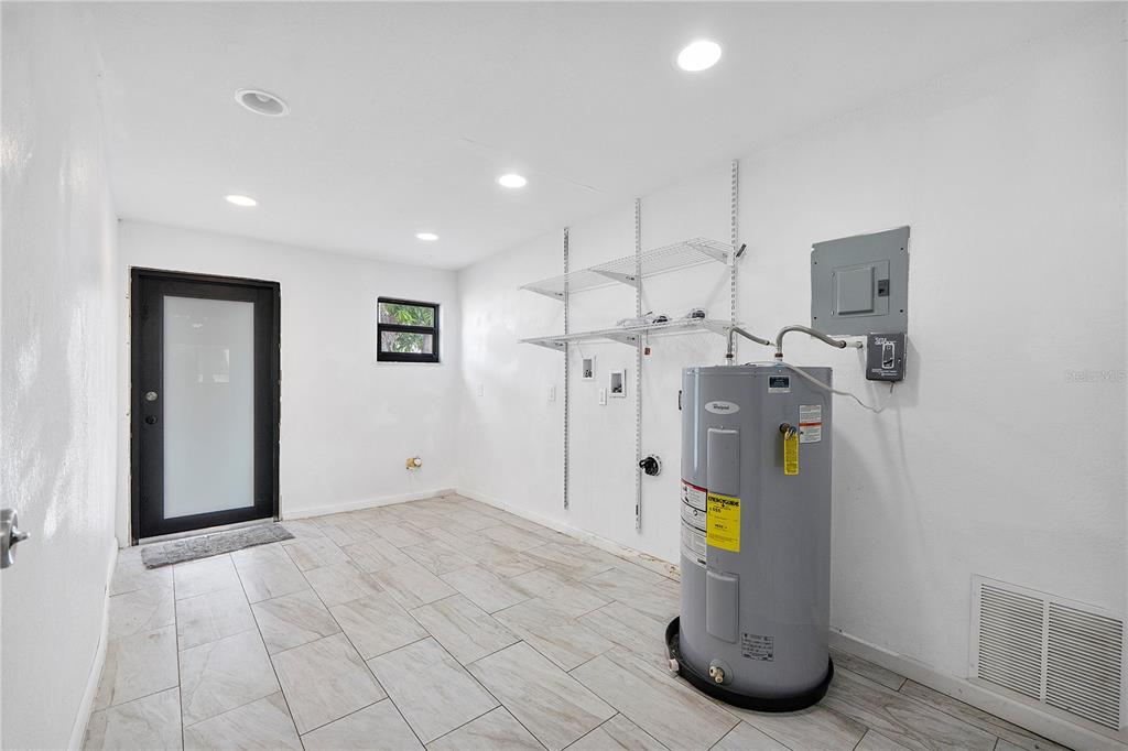 A utility room features white walls, tile flooring, a water heater, and wall-mounted wire shelving — 16011 NW 40TH COURT, MIAMI GARDENS, FL