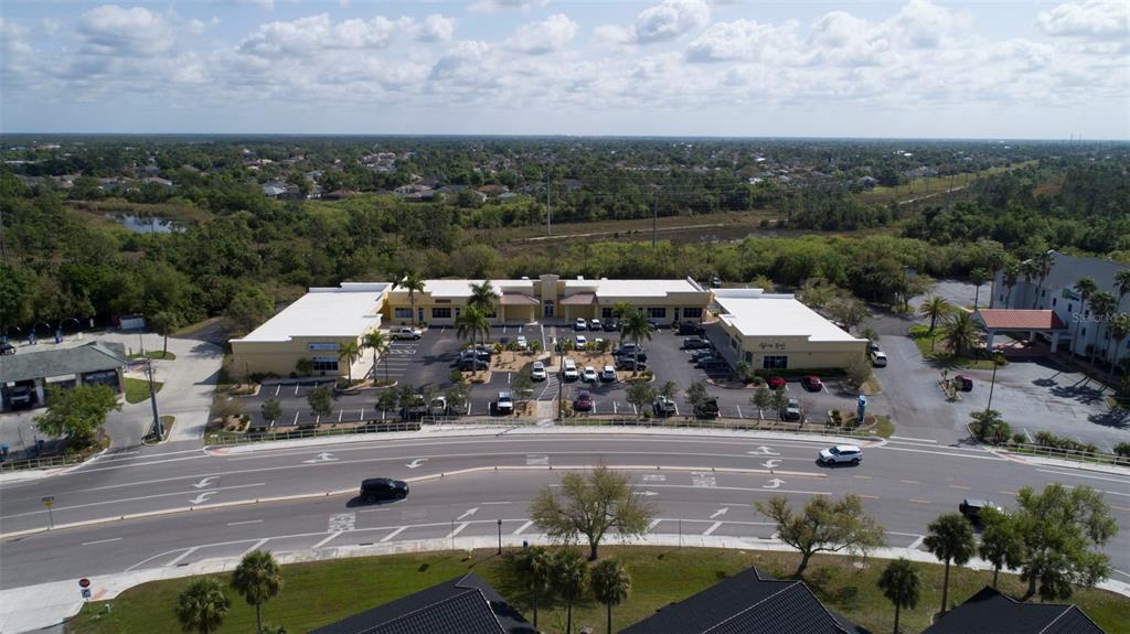 An aerial view shows a commercial plaza with a parking lot and surrounding landscape — 24420 SANDHILL BOULEVARD, PUNTA GORDA, FL